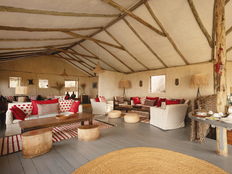 Spacious interior of a luxury safari tent with white sofas, red pillows, and rustic wooden beams.
