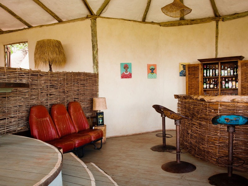 A rustic interior bar area with a woven stick counter, vintage red leather seats, and a wooden liquor cabinet.