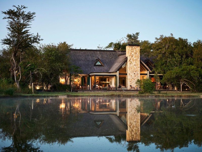 Thatched main lodge reflected in the waterhole at dusk, Monwana Game Lodge