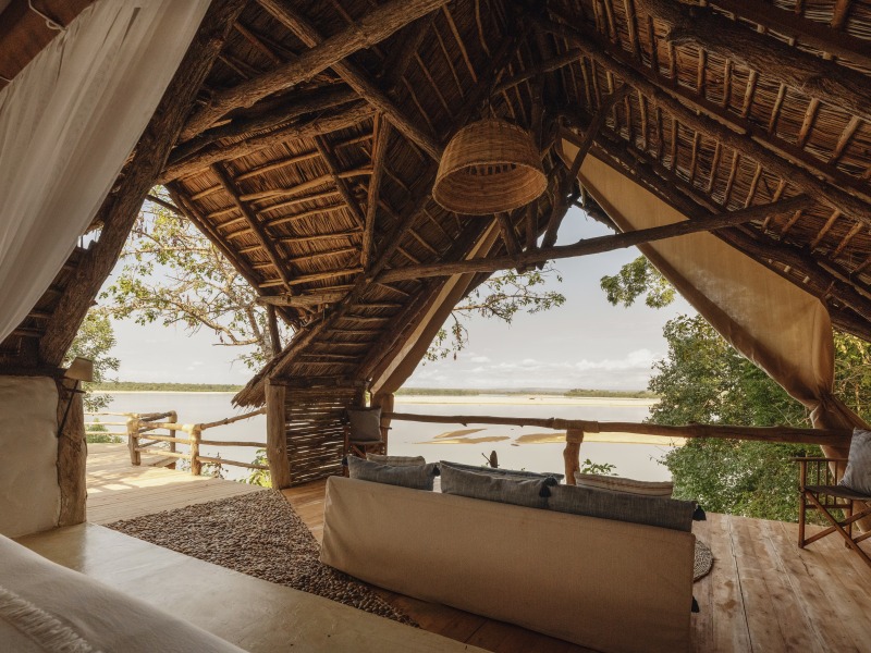 A luxury safari suite with a thatched roof and an open-air lounge area overlooking a wide river.