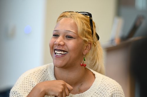 Portrait photo of a panel member smiling, wearing a white jumper with glasses on their head.