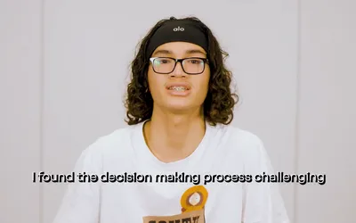 A youth panellist in a production studio wearing a white t-shirt and black glasses talks to camera