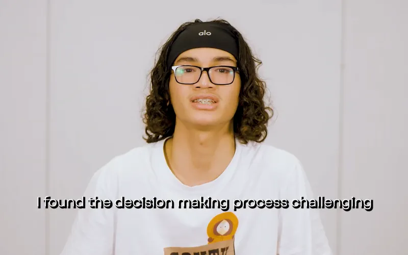 A youth panellist in a production studio wearing a white t-shirt and black glasses talks to camera