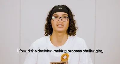 A youth panellist in a production studio wearing a white t-shirt and black glasses talks to camera