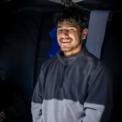 A team member of the wrap or rice box stall in Torrington Square smiles. He wears a dark blue fleece and you can see the dark material of the marquee in the background.