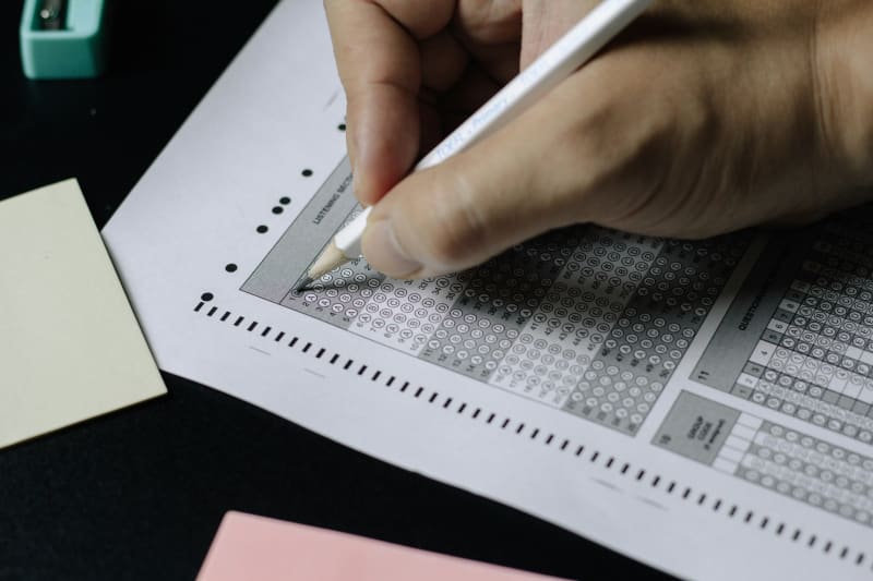 Student writing English language test at desk with study materials