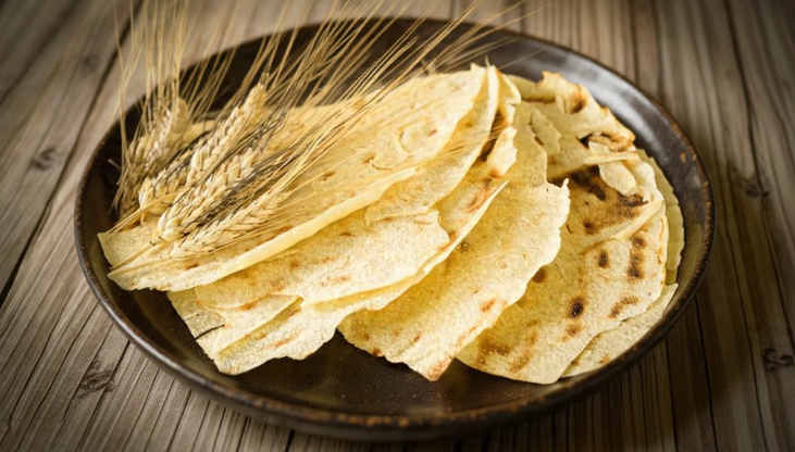 Thin crisp sheets of pane carasau stacked on a linen cloth with rosemary