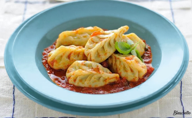 Handmade cullurgiones pasta with wheat-ear stitching on a rustic wooden board