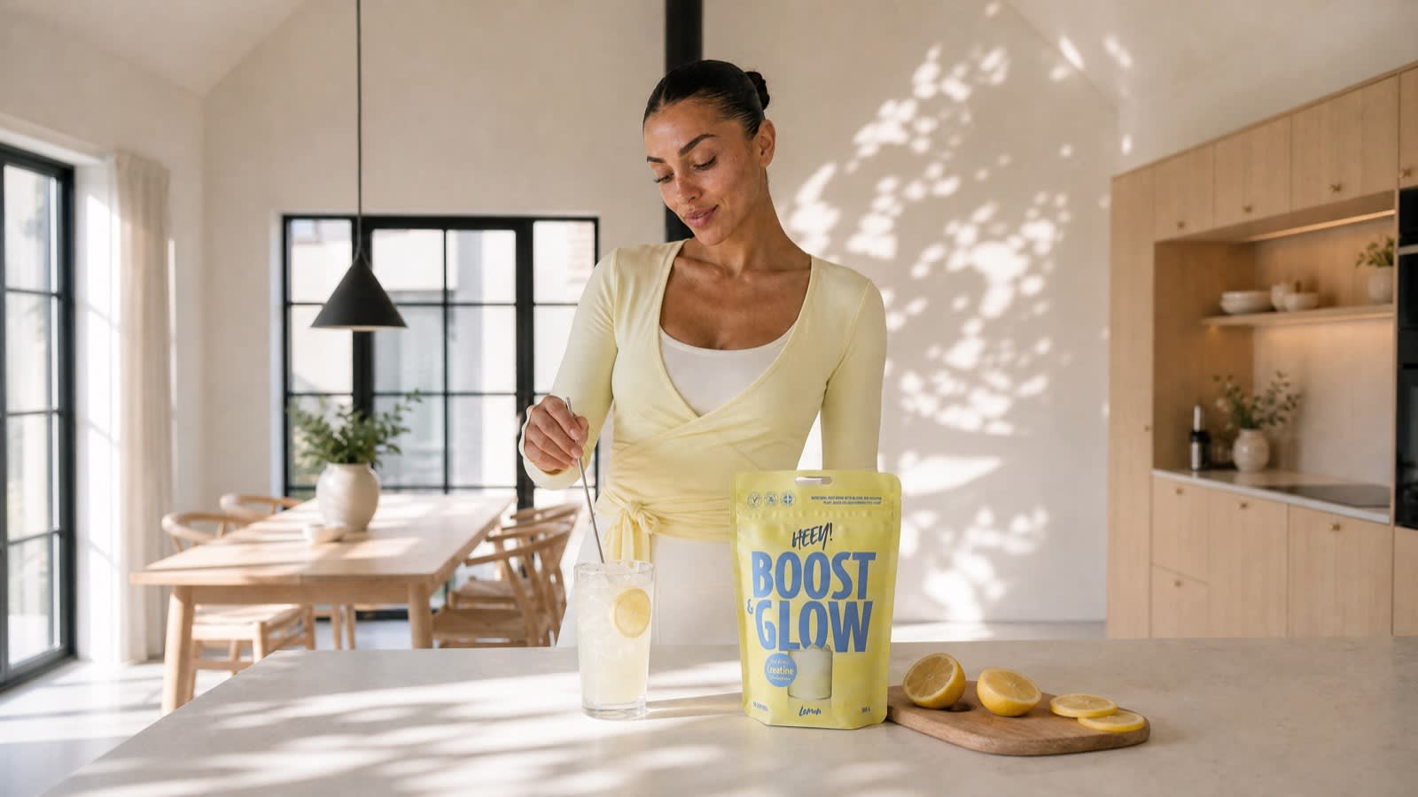 Kvinna rör om Boost & Glow Lemon i ett glas lemonad i ett ljust kök, vegansk kreatin för kvinnor