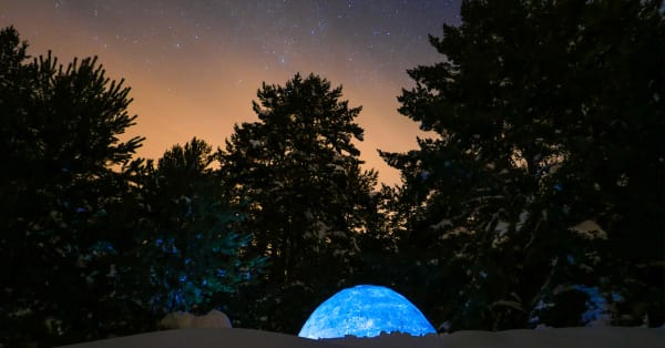 Aurora borealis illuminating a snowy hillside with a small igloo