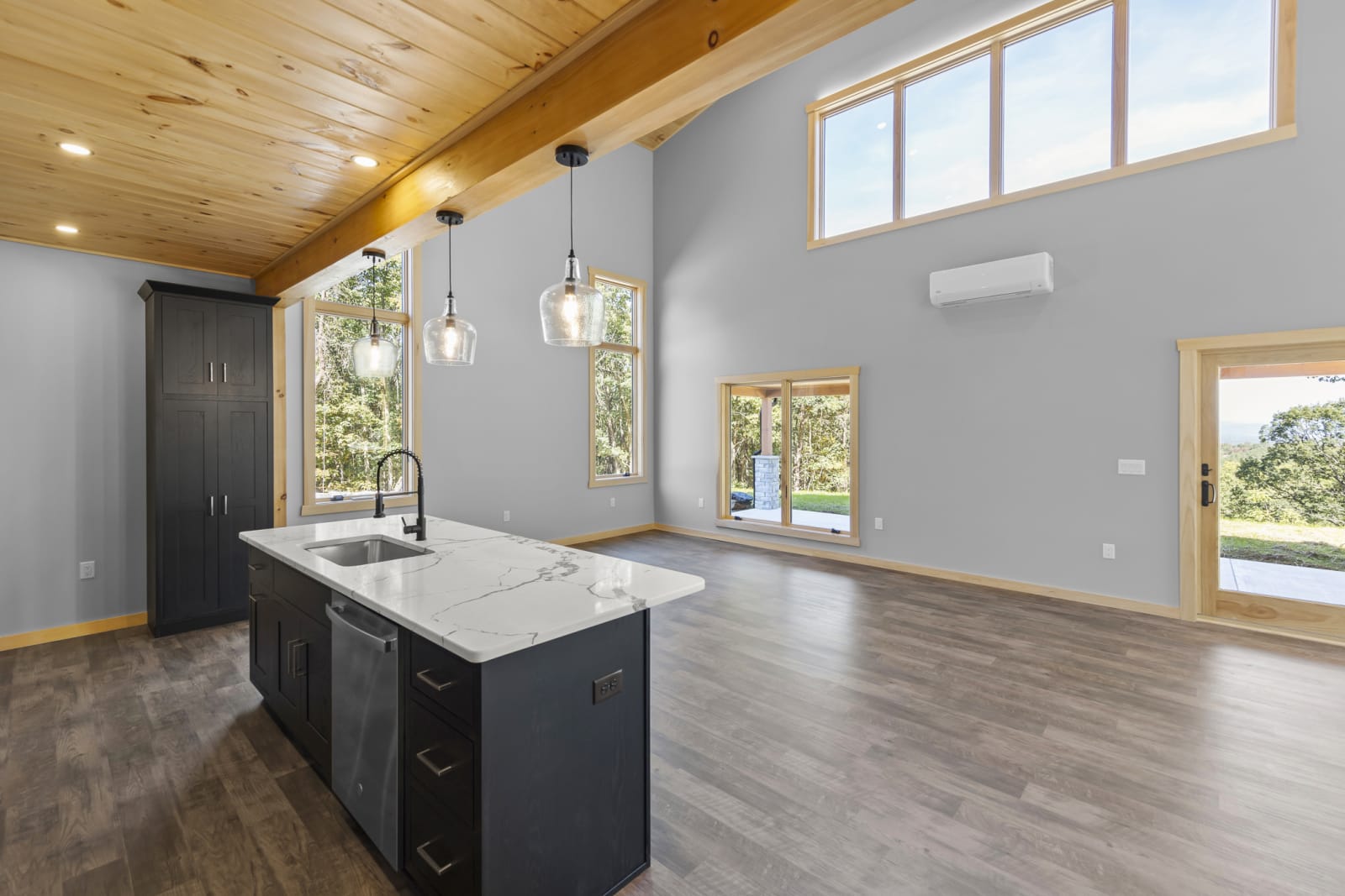 Open living room with vaulted pine ceiling, stone fireplace, and large windows