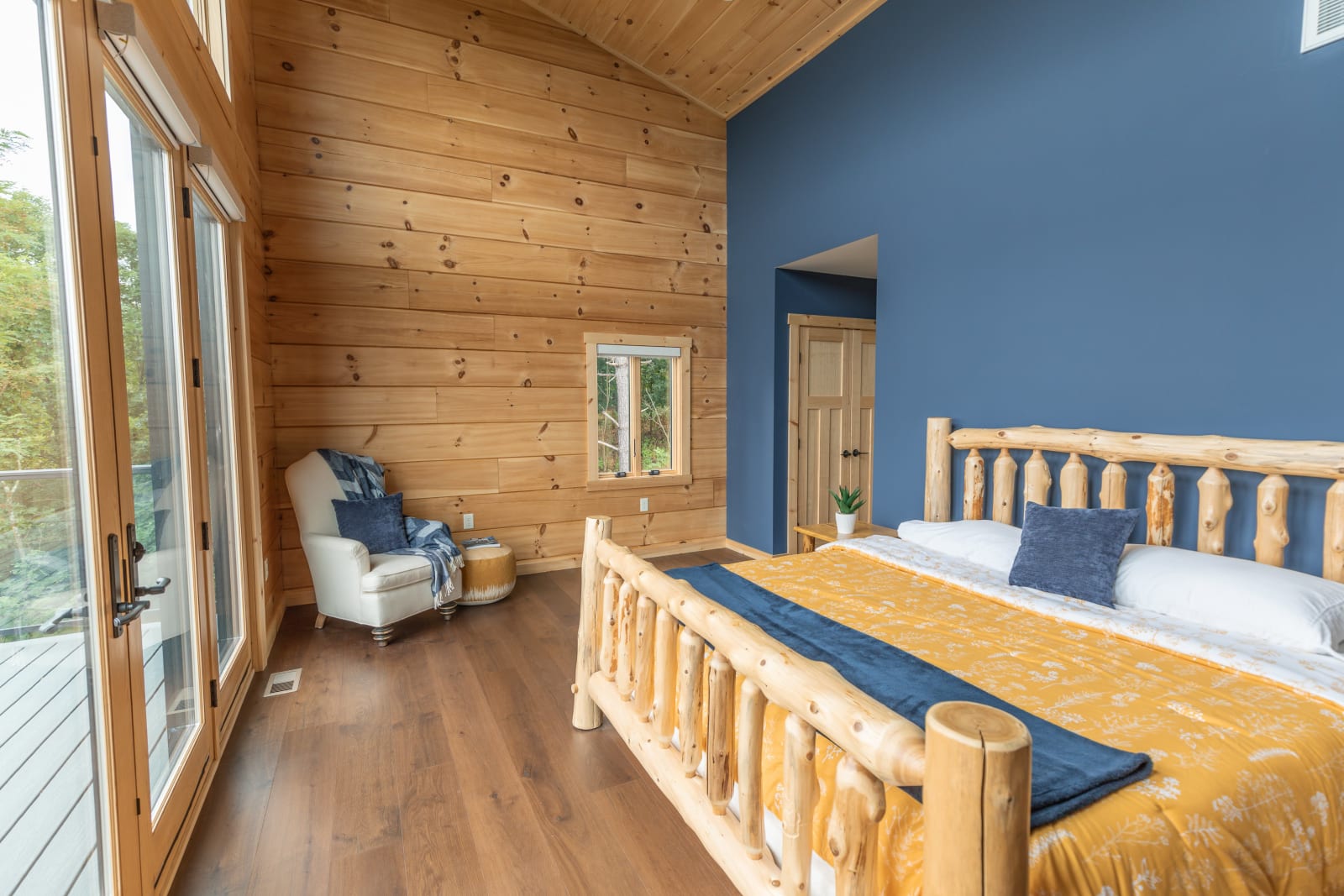 Bedroom with log walls, four-poster wooden bed, blue accent wall, and large windows