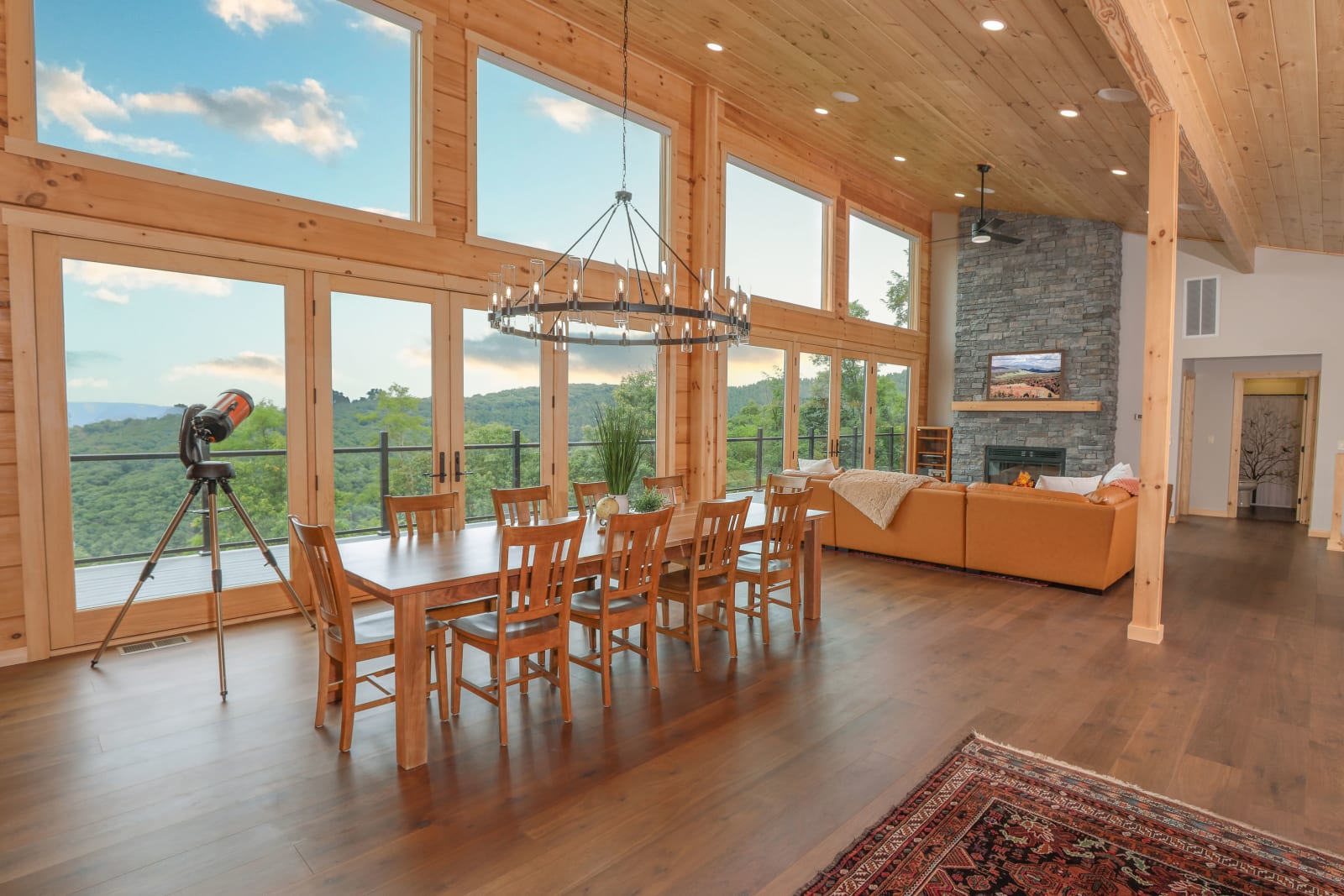 Open-concept living area with timber ceiling, stone fireplace, and wide-plank floors