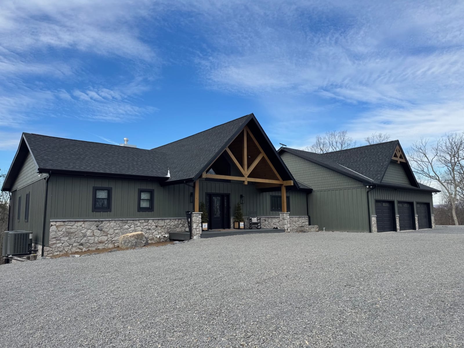 Front exterior of the Labuski hybrid home with dark green siding, stone base, and exposed timber entry trusses