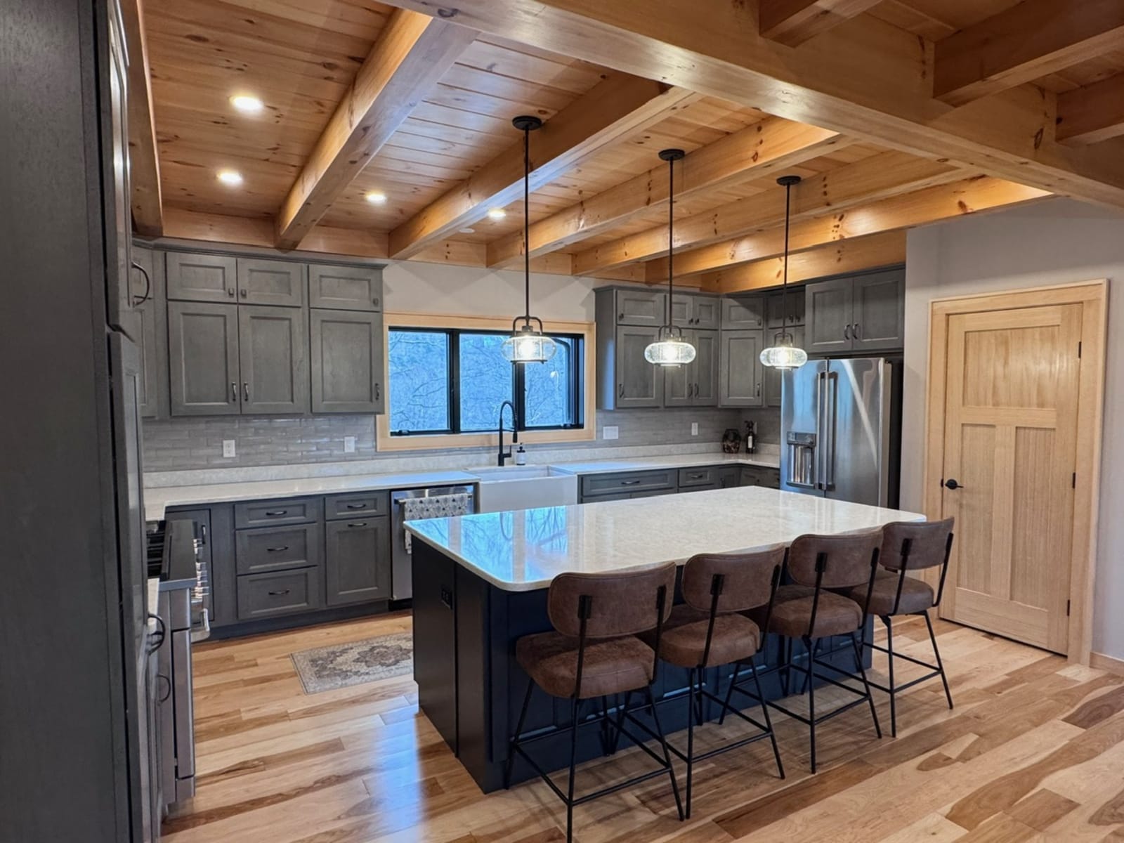 Kitchen with gray cabinets, white quartz island with bar seating, and exposed timber beam ceiling