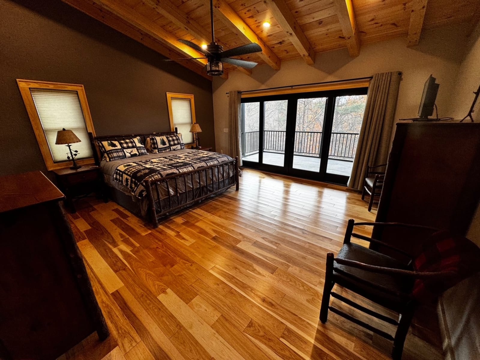 Master bedroom with timber beam vaulted ceiling, hardwood floors, and sliding glass doors to a wooded deck
