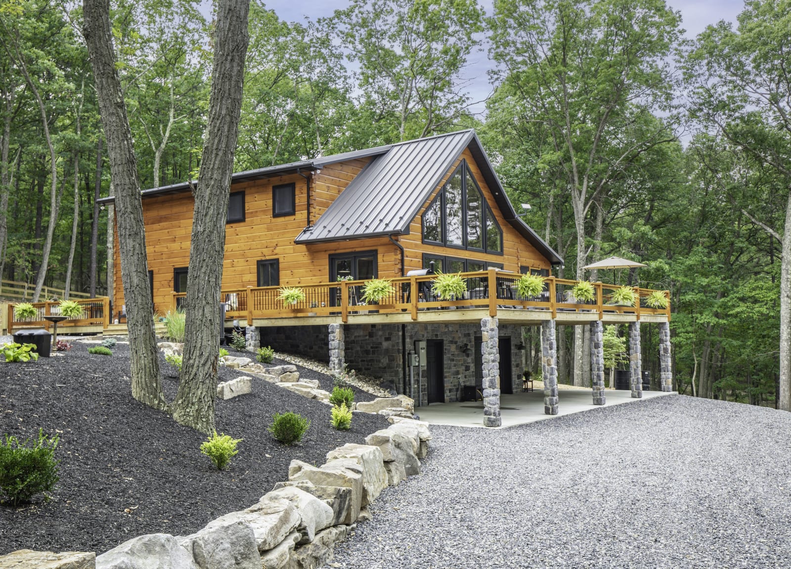 Ground-level exterior showing engineered log walls, stone landscaping, and covered entry