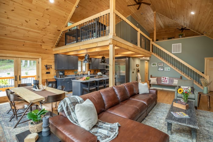 Great room with exposed log walls, stone fireplace, and loft overlook
