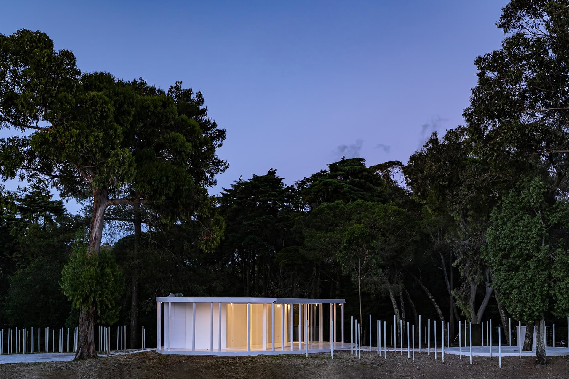 6-Vila-Lisboa-Lisboa - Aclamado por todos como o pulmão verde de Lisboa, Monsanto tem estado, de certa forma, abandonado à deterioração natural, carecendo de estruturas funcionais e apelativas de apoio aos habitantes da cidade de Lisboa. A par das novas tendências do estilo de vida dos portugueses, nomeadamente dos residentes nas grandes cidades, verifica-se uma procura crescente de espaços verdes, quer para a prática de desportos, quer para atividades de lazer ou apenas para usufruto e maior contacto com a natureza. Monsanto não é exceção, não obstante a falta de condições do parque florestal.
Monsanto tem uma nova “Floresta Branca”. Correspondendo às expectativas de muitos lisboetas, após um longo período de espera, vários projetos de requalificação estão a ser desenvolvidos pela Câmara Municipal de Lisboa e Juntas de Freguesia em diferentes zonas de Monsanto. A Junta de Freguesia de Benfica abriu um concurso público de reabilitação, o contrato entregue à Empresa CVZ Construções, que, em parceria com o gabinete de Arquitetura Bruno Câmara Arquitetos, desenvolveu todo o projeto de Concepção e Construção de um novo restaurante/bar com zonas exteriores, incluindo vários percursos pedonais e espaços lúdicos. Bruno Câmara Arquitectos adotou o conceito de “Uma Floresta Branca”, para criar um Projeto globalmente marcado pela cor branca, seguindo linhas minimalistas de Arquitetura Moderna e Contemporânea. Segundo o Arquiteto Bruno Câmara, Autor do Projeto,  o conceito “materializa todos os elementos propostos, integrando os mesmos no enquadramento paisagístico de Monsanto. 3.411 troncos de madeira pintados a branco formam vários espaços exteriores com diferentes funções, desde pequenos auditórios a espaços de lazer, envolvendo o espaço principal de restaurante/bar com a zona interior e exterior, que valoriza a espacialidade e ligação à natureza envolvente.”
A nova construção destaca-se assim pelo seu branco minimalista inserido no verde de Monsanto, que cria harmonia com os espaços envolventes, quer pelas suas linhas curvas, quer pelos materiais utilizados, conferindo-lhes modernidade.