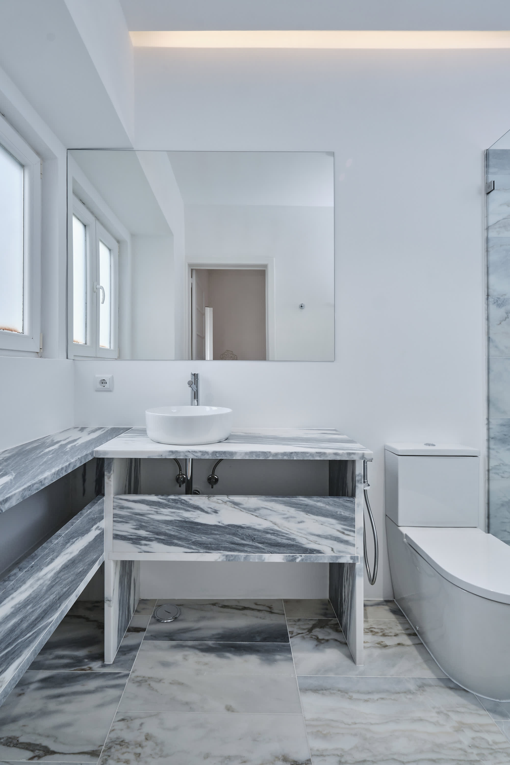 17-Apartamento-Lisboa-Lisboa - O apartamento insere-se num edifício de gaveto entre a Avenida de Berna e Avenida Marquês de Tomar no bairro das Avenidas Novas, localizado na zona central de Lisboa, junto à Avenida da República, uma das principais vias da cidade. A Avenida de Berna tem uma longa história de Glamour e estilo de vida de classe alta e essa cultura esteve presente na nossa forma de abordar o Projeto.
O bairro é definido por vias largas de dois sentidos, logradouros ajardinados e coerência estética no desenho das fachadas, tornando Avenida de Berna numa das zonas mais valorizadas de Lisboa. O edifício  é composto por um piso térreo e quatro pisos seguintes. A construção é definida por fundações em alvenaria de pedra, que é o mesmo material presente nas paredes exteriores. Os interiores por si, encontram-se em tijolo maciço, com uma laje mista e cobertura em telha marselha assente em barrotes de madeira. São criadas novas aberturas interiores, o layout da cozinha é alterado para permitir a continuidade e fluidez espacial entre o espaço social definido pelas divisões conectadas.
O alçado principal é definido por uma métrica de vãos com de guardas metálicas, assim como vãos exteriores em alumínio com vidro duplo e com uma cobertura de duas águas em cerâmica. Com a intervenção da CVZ Construções, nasce uma nova zona social. Uma nova disposição, com maior espacialidade e luminosidade, na cozinha, sala e Instalações Sanitárias. O novo espaço traz mobiliário fixo de biblioteca e zonas de iluminação indireta.