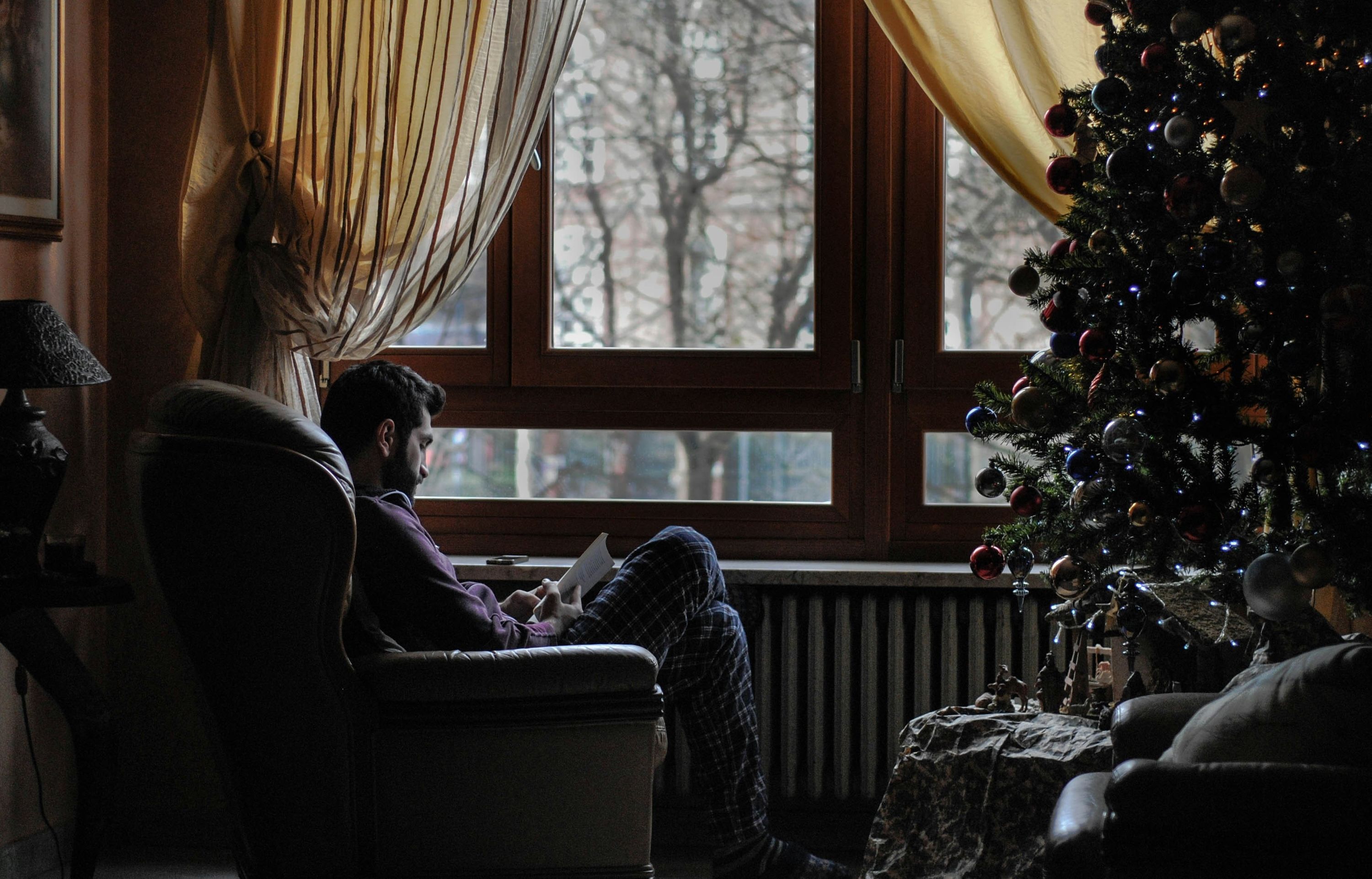a man reading a book by a window next to a tree