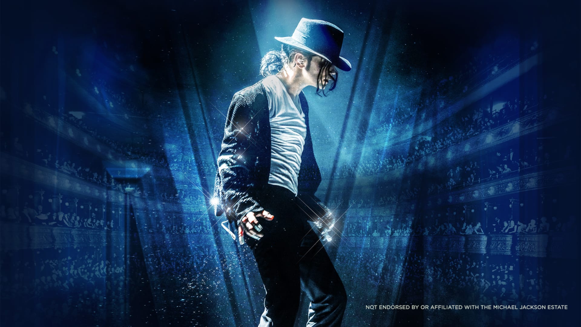 A performer in a black fedora, sequinned jacket and white t-shirt strikes a bent-forward pose under blue stage lighting with a blurred crowd behind.