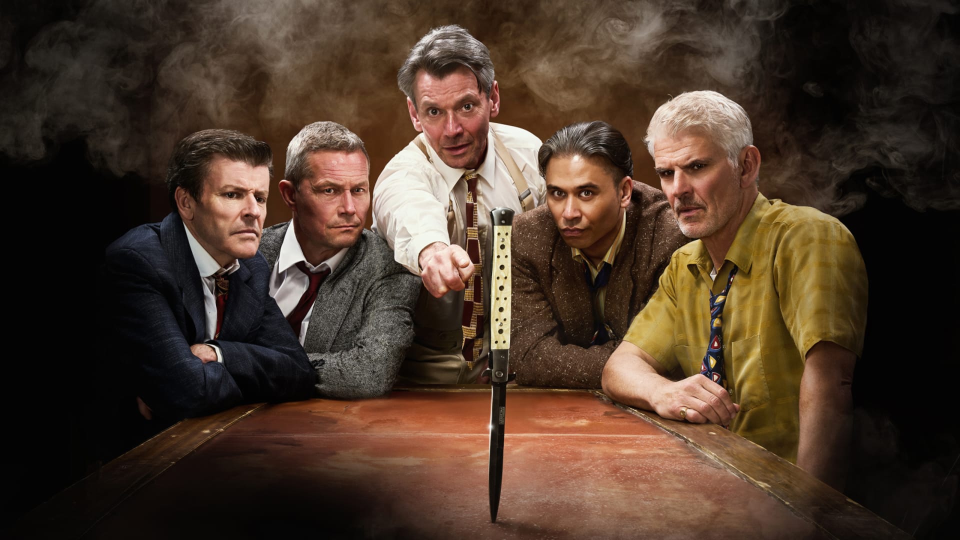Five men in mid-century suits and shirtsleeves lean over a wooden table, one pointing a switchblade knife downward into its surface, against a dark smoky brown background.