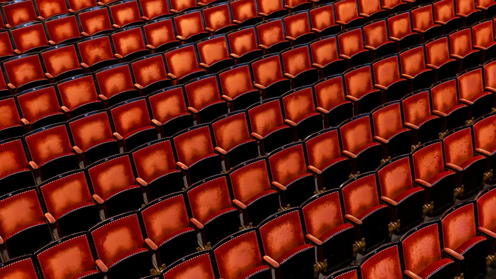 Rows of deep red upholstered theatre seats with dark wooden frames, viewed from above at an angle, filling the entire frame