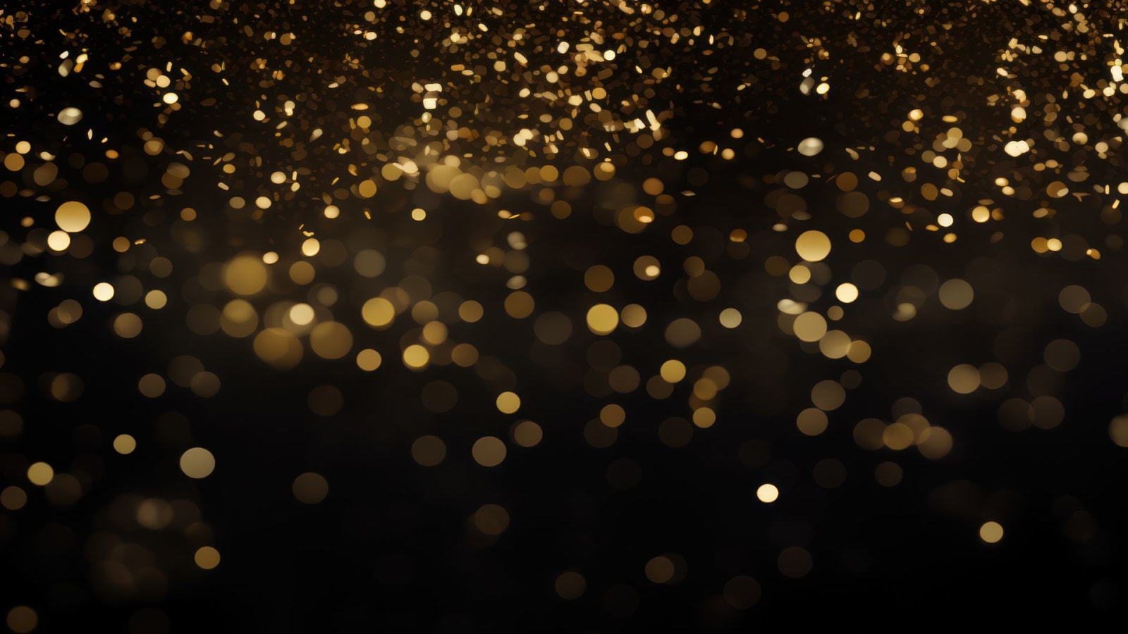 Gold confetti particles scattered out of focus against a black background.