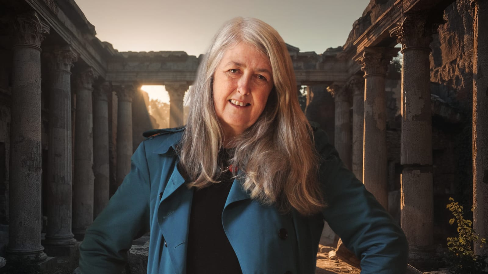 A woman with long grey hair wearing a teal coat stands with hands on hips among ancient stone columns and ruins, with golden sunlight breaking through an archway behind her.