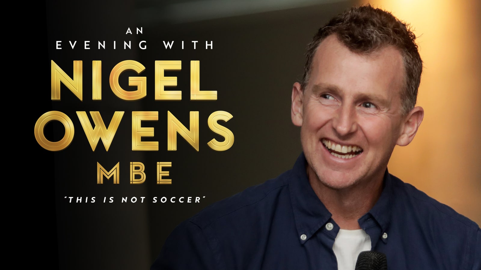Promotional graphic reading 'An Evening with Nigel Owens MBE – This Is Not Soccer' in gold lettering on a dark background, alongside a man in a navy shirt holding a microphone and smiling.