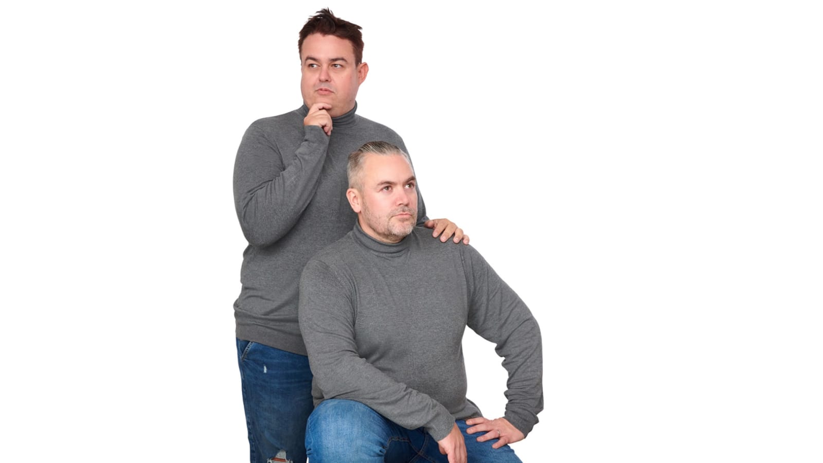 Two men in matching grey roll-neck jumpers and blue jeans pose against a white background.