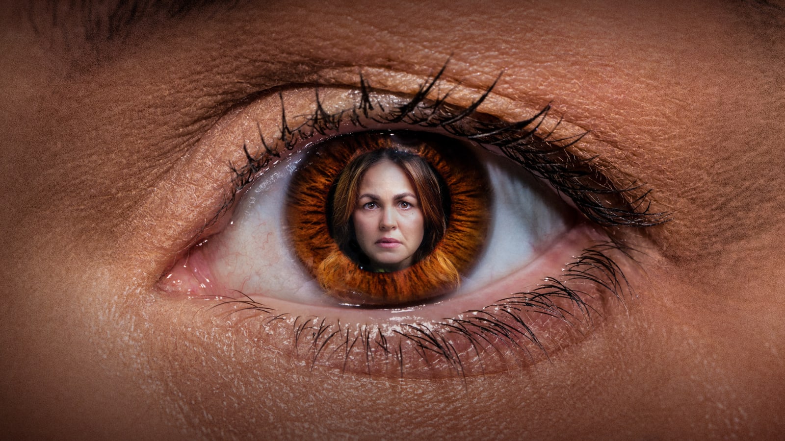 Extreme close-up of an amber-brown eye with a woman's face composited into the iris, set against warm skin tones.