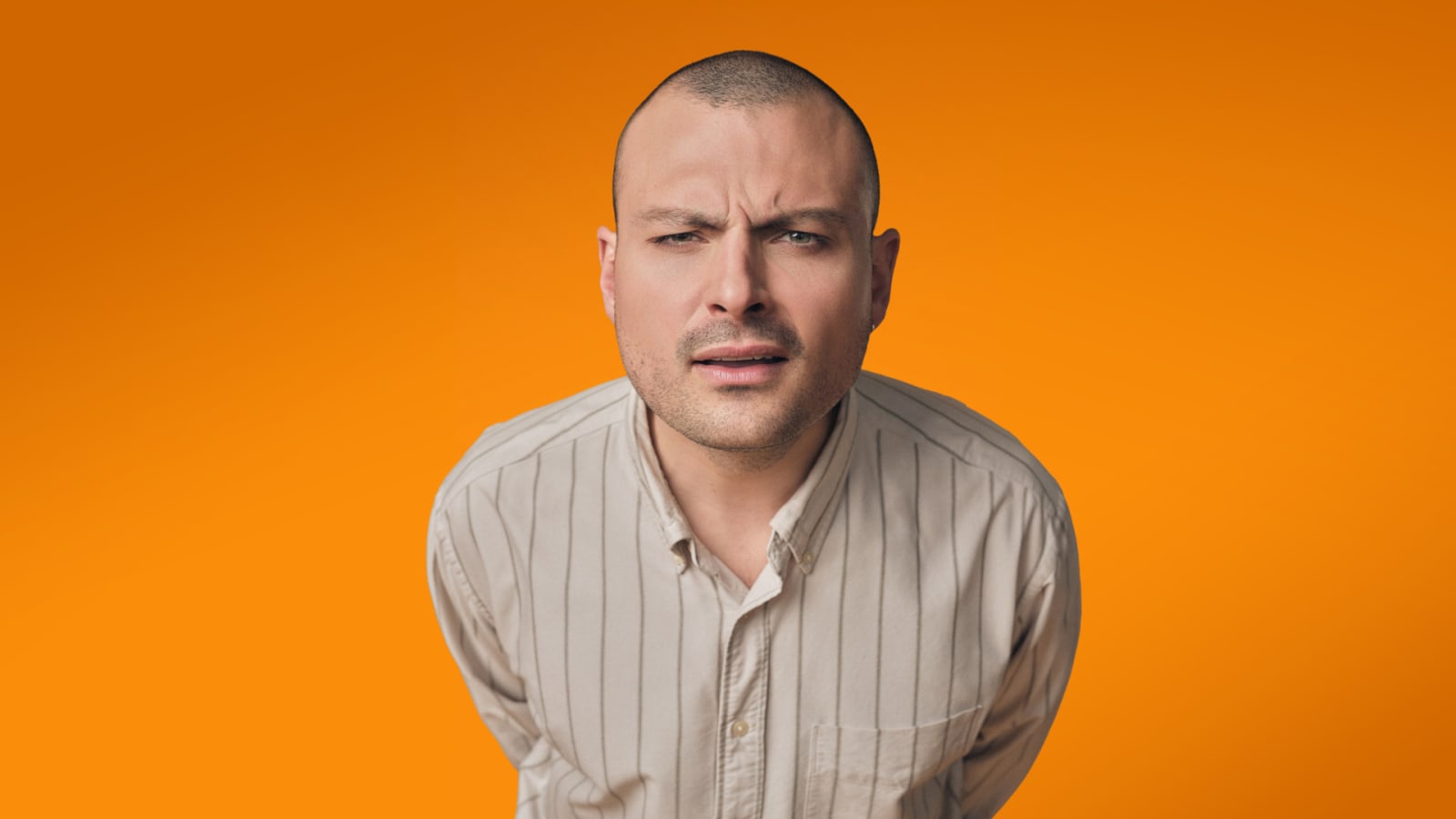 Promotional portrait of a man in a cream pinstripe shirt against a vivid orange background.
