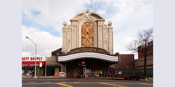 An exterior shot of Kings Theatre from across the street on Flatbush Ave. Kings Theatre's exterior is an ornate old theatre with a central marquee out front.