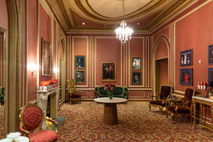 A shot of one of the premium lounges inside Kings Theatre. It is an historic room with an ornate carpet, lush furniture, a fireplace, and framed photos of past performances.