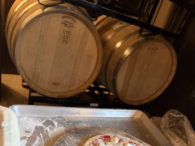 Unbaked pizza topped with sauce, shredded and cubed cheese, set on a floured peel near wine barrels