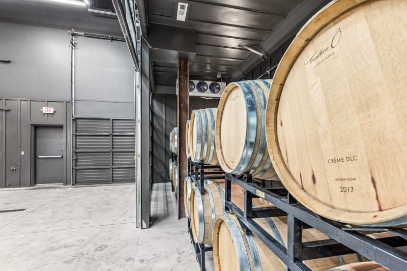Oak wine barrels on metal racks in a cellar, foreground barrel marked Crème DLC 2017.