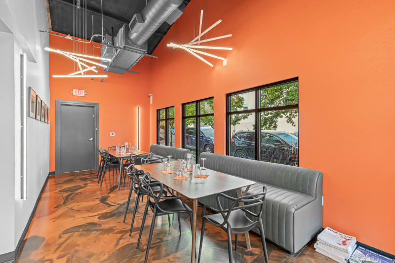 Tasting room with orange walls, gray booth seating, tables set with wine glasses, and large windows.