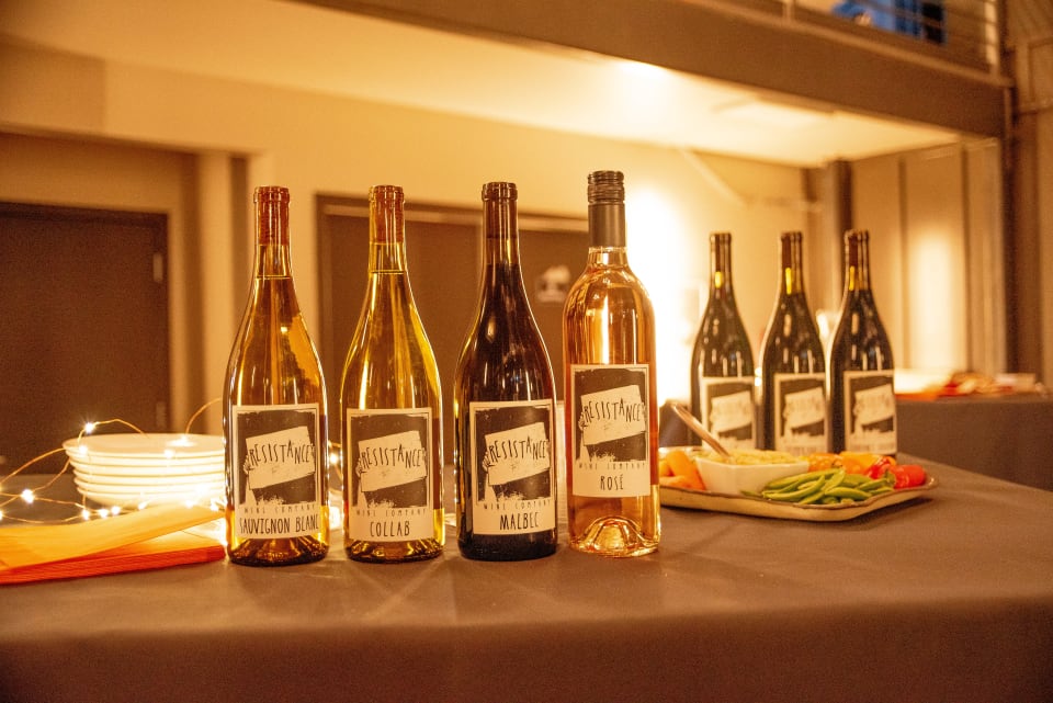Four Resistance SKUs — Sauvignon Blanc, Collab, Malbec, and Rosé — lined up on a draped event table with crudité and string lights.