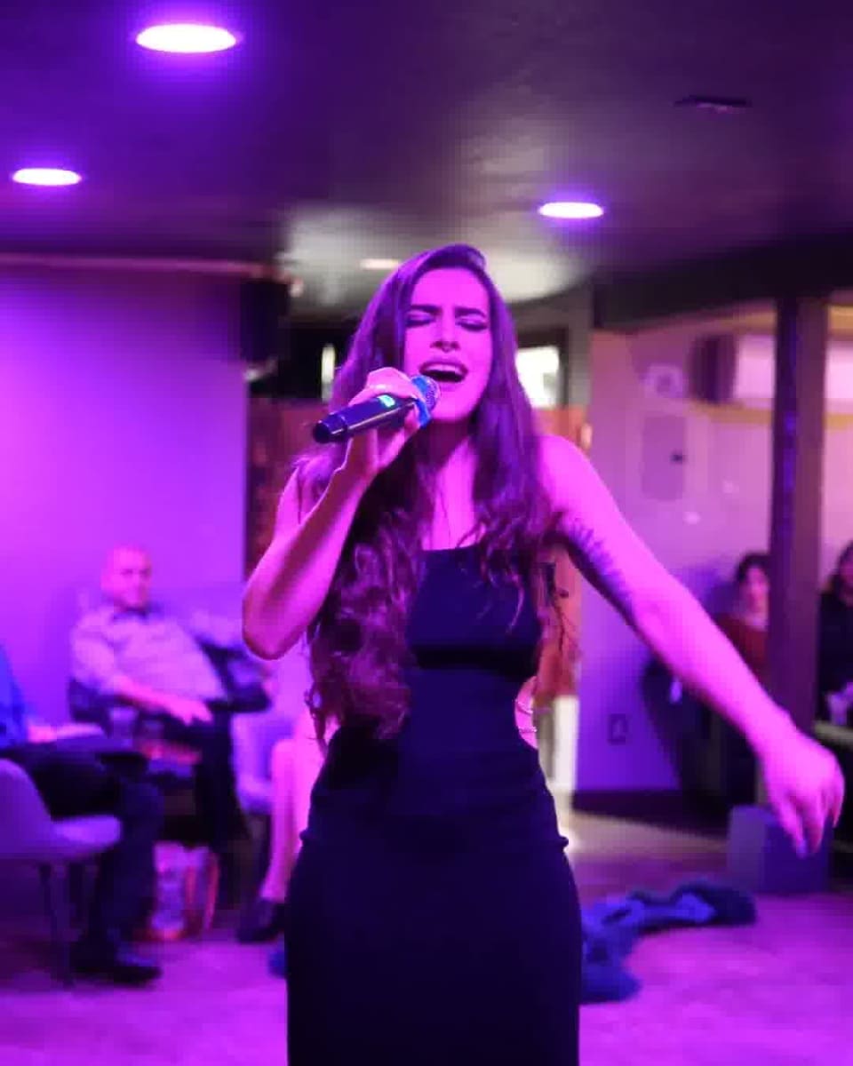 Victoria Lawton singing into a handheld microphone in a long black dress during a lounge performance