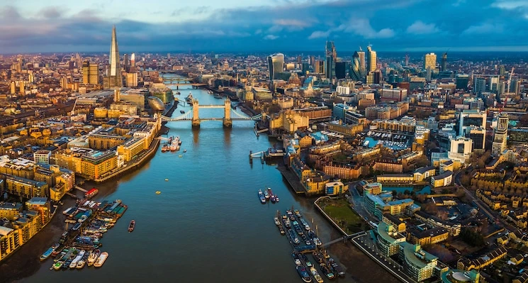 London, England – Panoramic aerial skyline view of London including Tower Bridge with red double-decker bus, Tower of London, skyscrapers of Bank District
