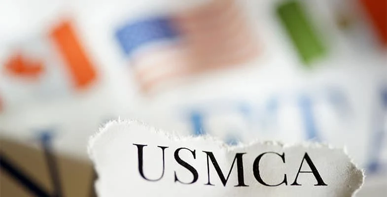 An close-up image of the text NAFTA, with the U.S, Canadian, and Mexico flags in the background.