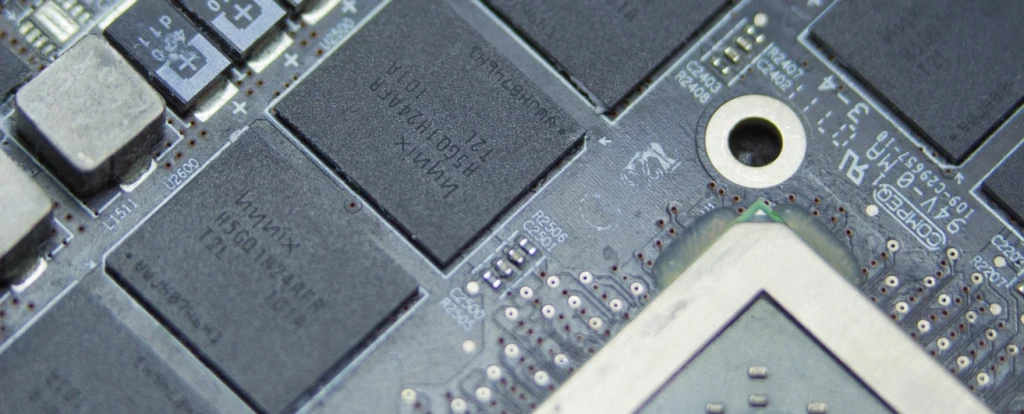 Close-up view of a computer circuit board featuring several black integrated circuits alongside capacitors and other electronic components. The board includes detailed etchings, a metallic screw hole, and intricate soldering points.