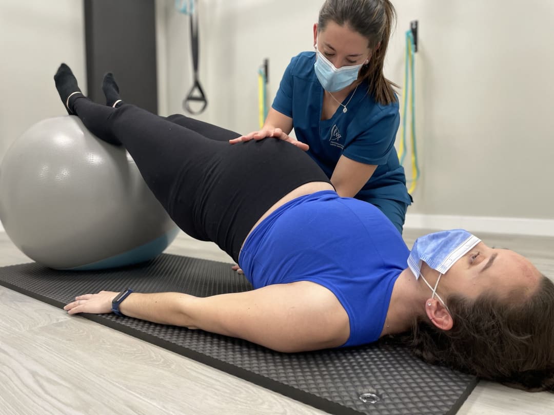 Mujer embarazada haciendo Pilates con fitball asistida por fisioterapeuta en Rivas
