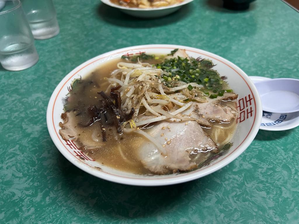A bowl of budget-friendly ramen sits on a green table, featuring rich broth, sliced pork, bean sprouts, seaweed, and green onions. This dish is one way to save money in Japan while enjoying authentic culinary delights. The vibrant ingredients offer a taste of traditional Japanese flavors without breaking the bank.