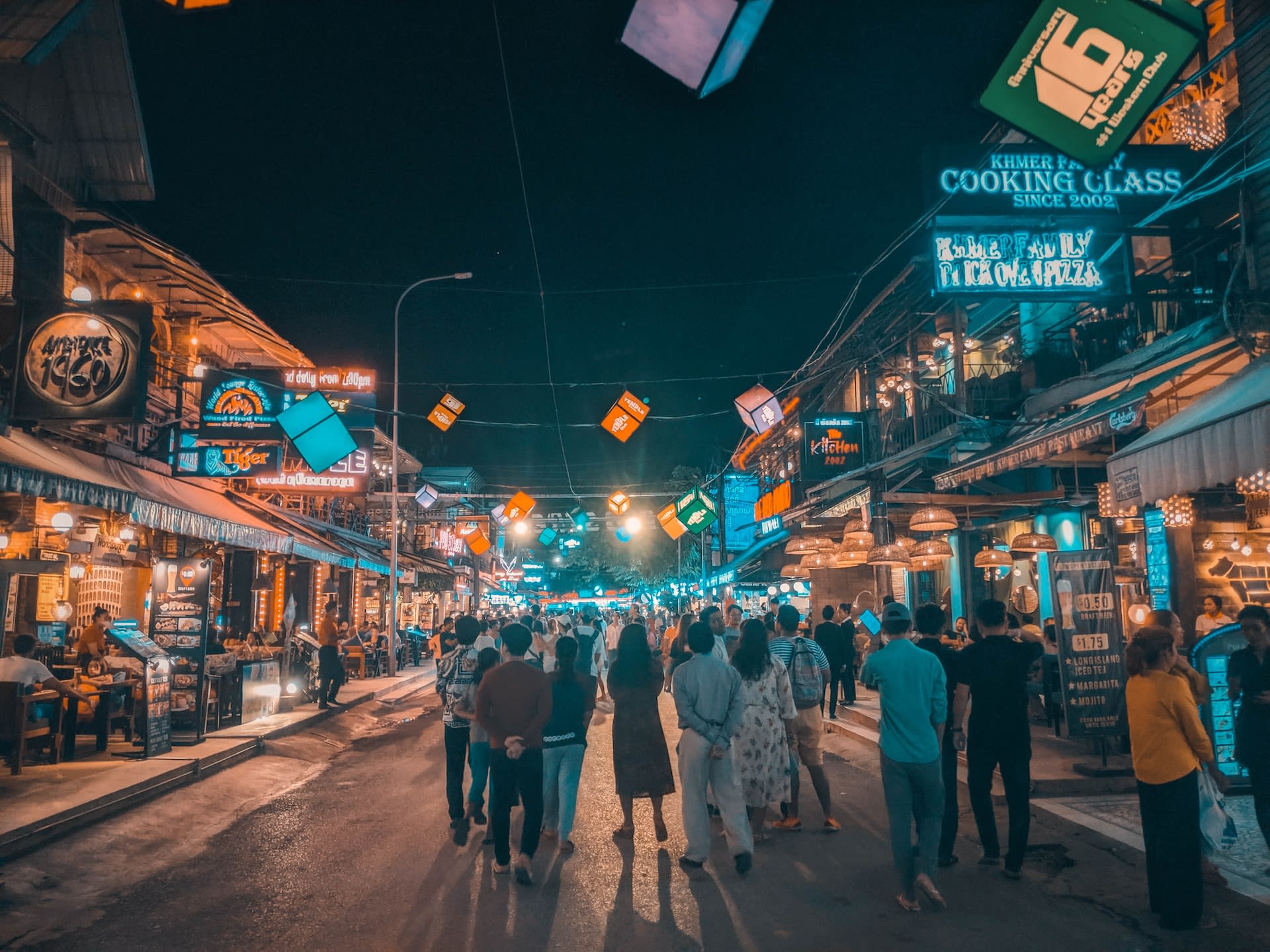People stroll through a lively street glowing with colorful signs and bustling shops, immersed in vibrant LGBTQ+ experiences. The neighborhood captures the essence of off-the-beaten-path gay cities with its unique charm and welcoming atmosphere, making it a hidden gem for visitors seeking an authentic taste of inclusive nightlife and culture.