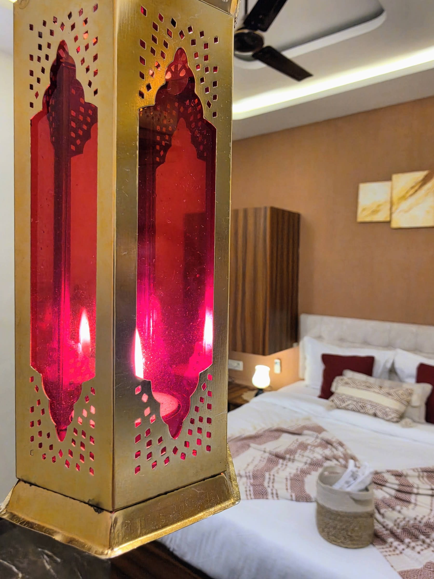 A brass lantern with red glass glowing beside a made-up bed in a guest room