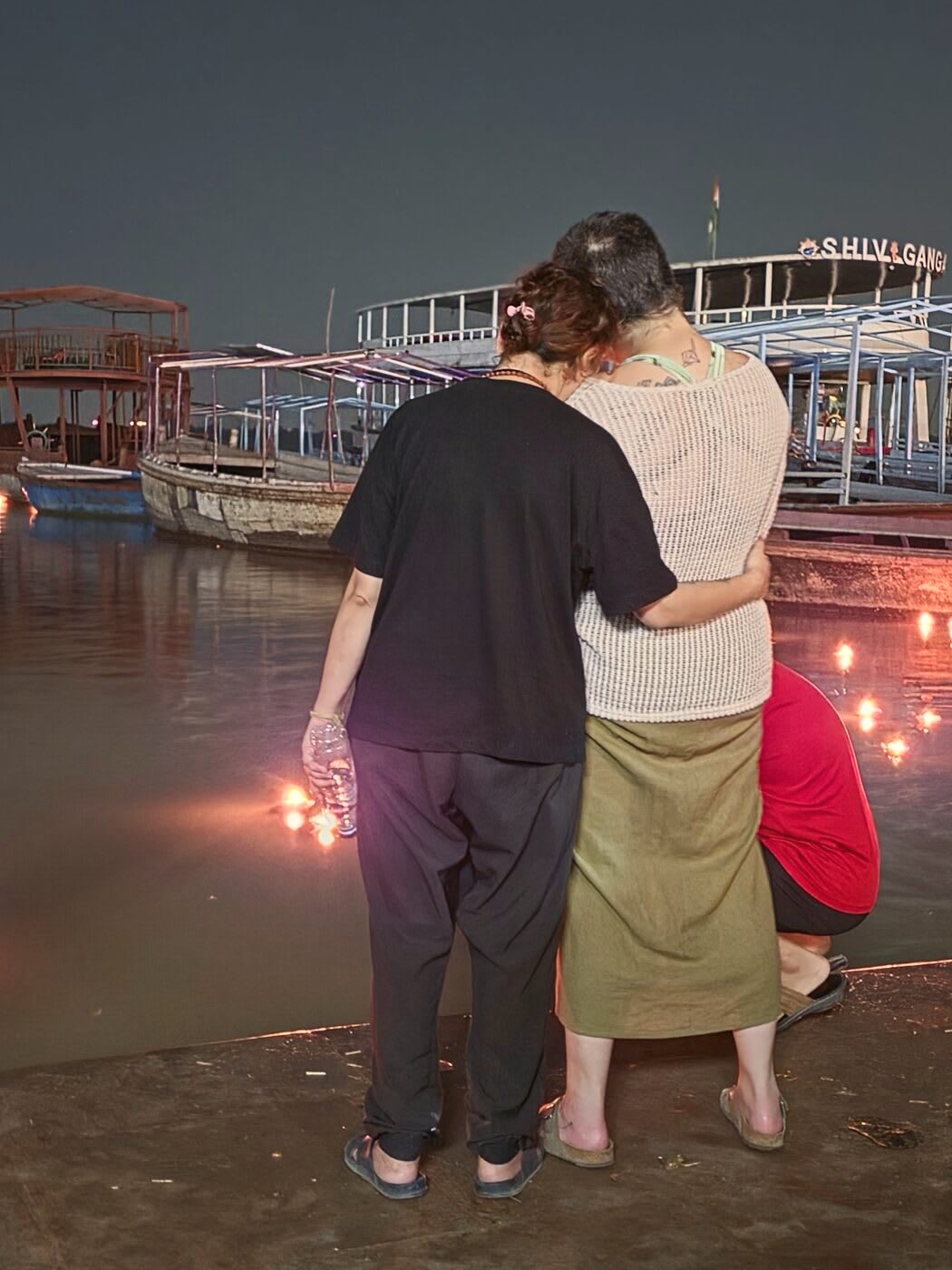 Two of us arm in arm at the river's edge at night, floating lamps on the water
