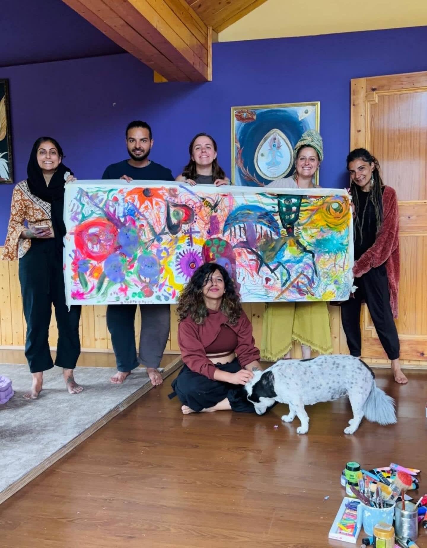Guests holding up a large colourful painting they made, with the house dog in front